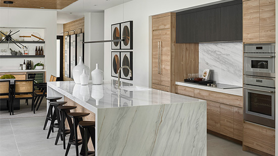 Open-plan kitchen with wood-grain tall units, a dark upper run and a marble waterfall island with black bar stools